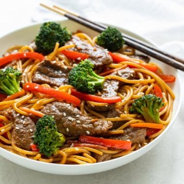 Closeup view of beef and broccoli lo mein in a white bowl with chopsticks.