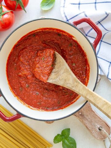 Overhead view of a wooden spoon in a red pot of homemade marinara sauce.