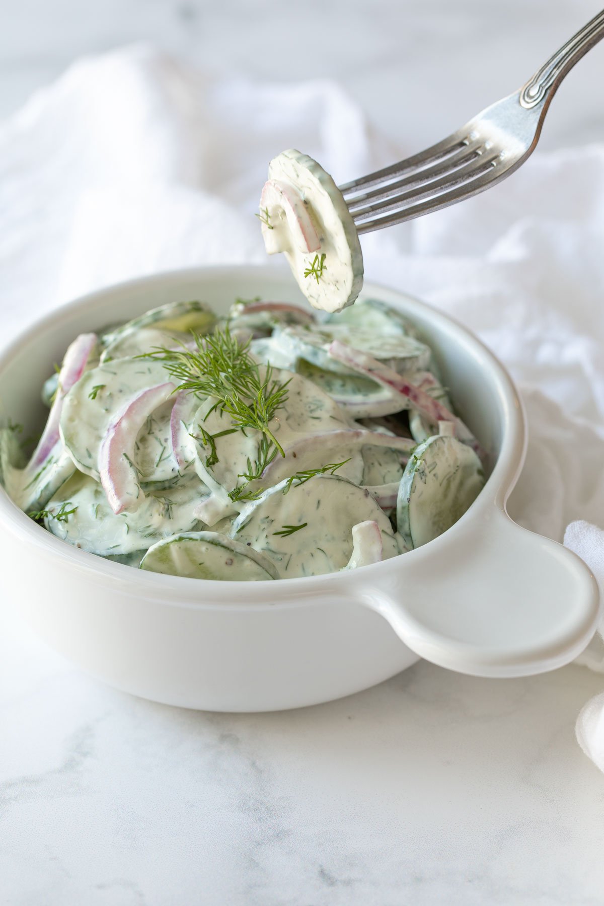 A fork holding a slice of cucumber and onion over a bowl of German cucumber salad.