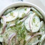German cucumber salad in a white bowl with overlay text.