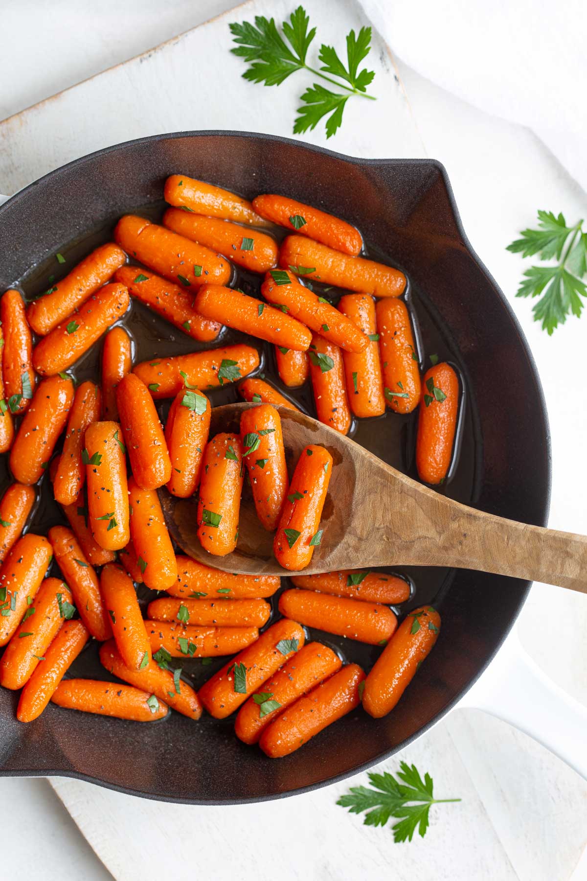 Overhead view of maple glazed carrots in a skillet with a wooden spoon.