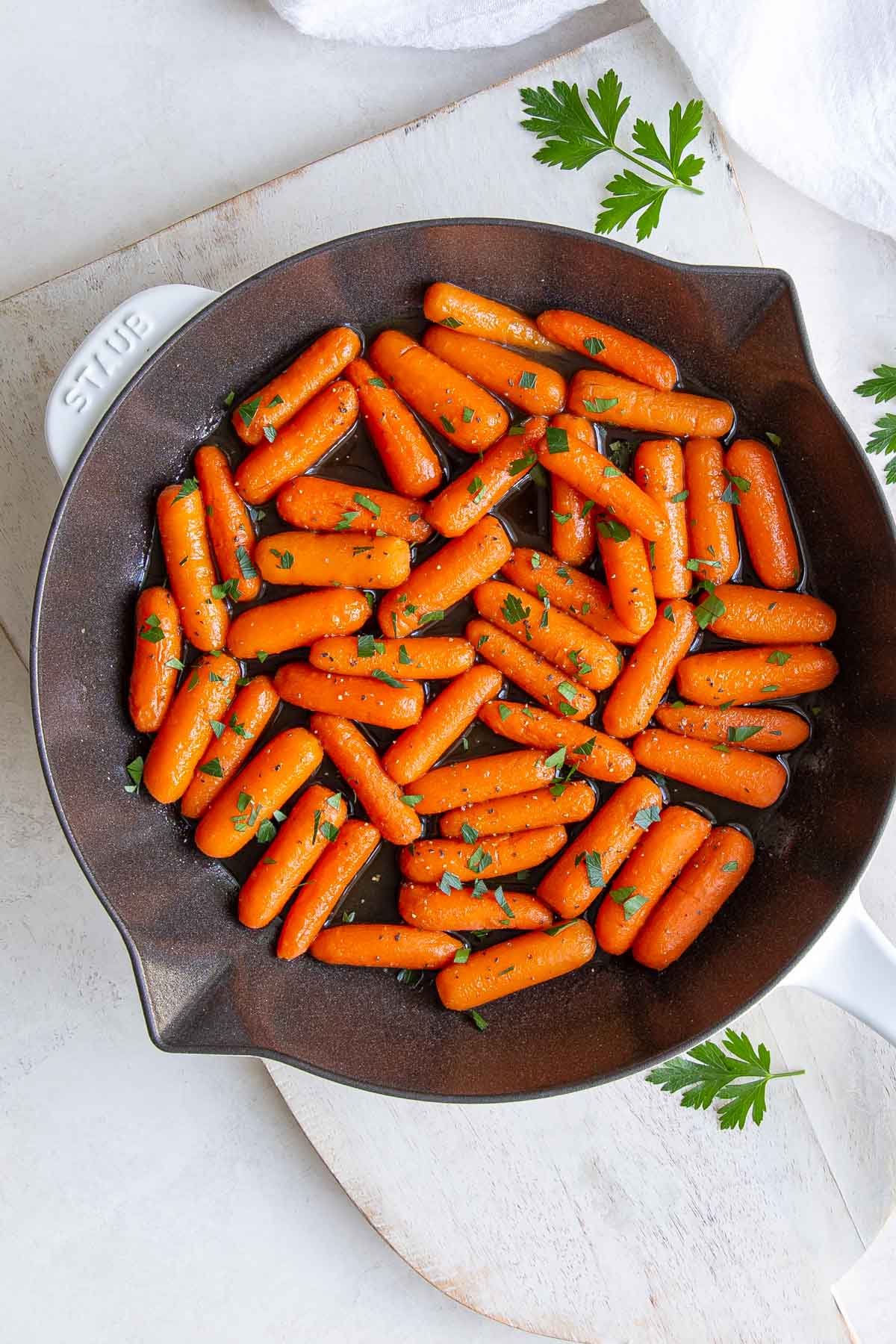 Overhead view of maple glazed carrots in a skillet on a white wooden cutting board.
