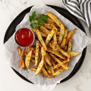 Air fryer French fries on a black plate lined with parchment paper.