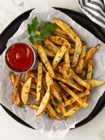 Air fryer French fries on a black plate lined with parchment paper.