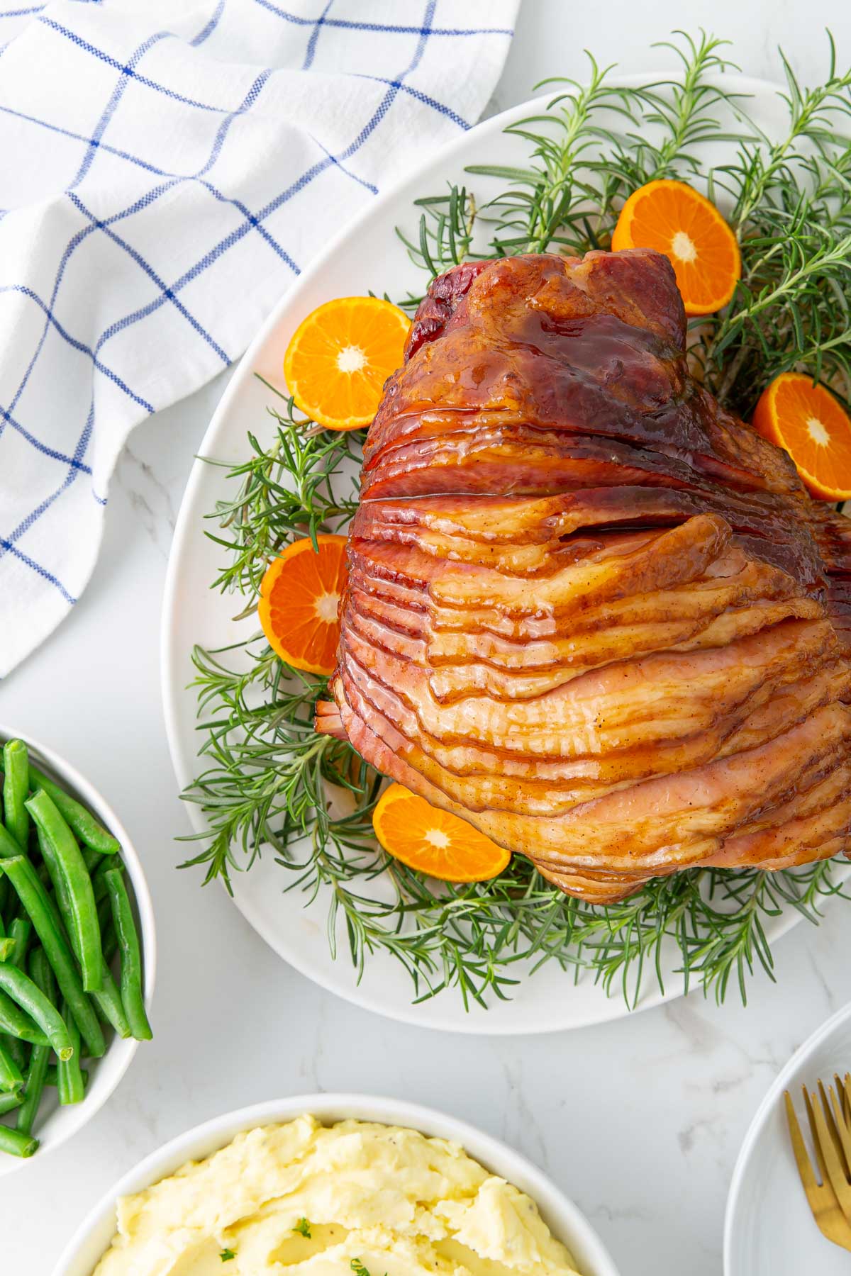 Overhead view of a glazed spiral ham beside a bowl of mashed potatoes and a bowl of green beans.