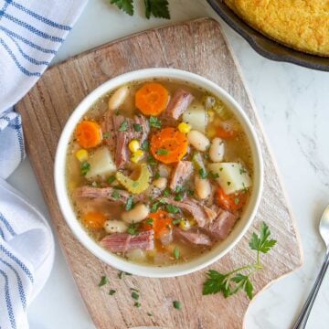 Overhead view of slow cooker ham bone soup in a white bowl beside a skillet of cornbread.