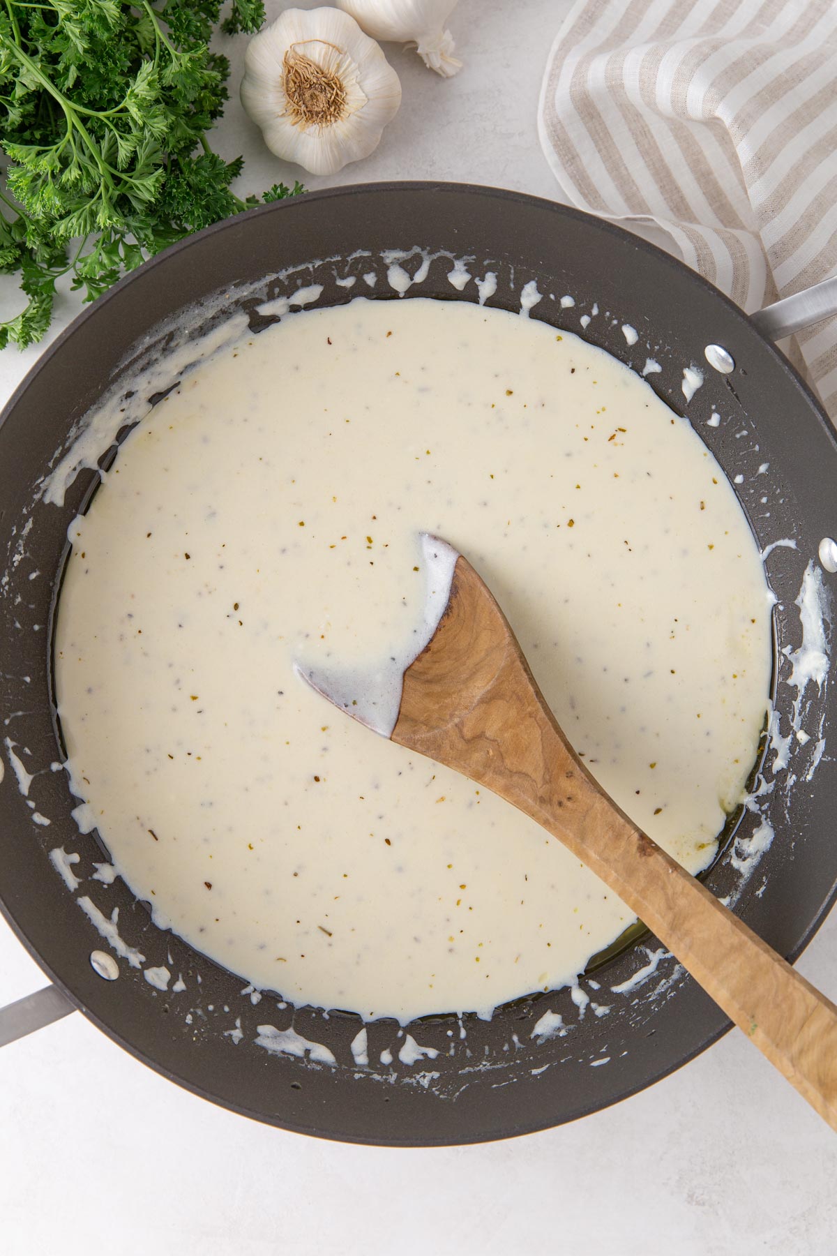 Overhead view of Alfredo sauce in a pan with a wooden spoon.