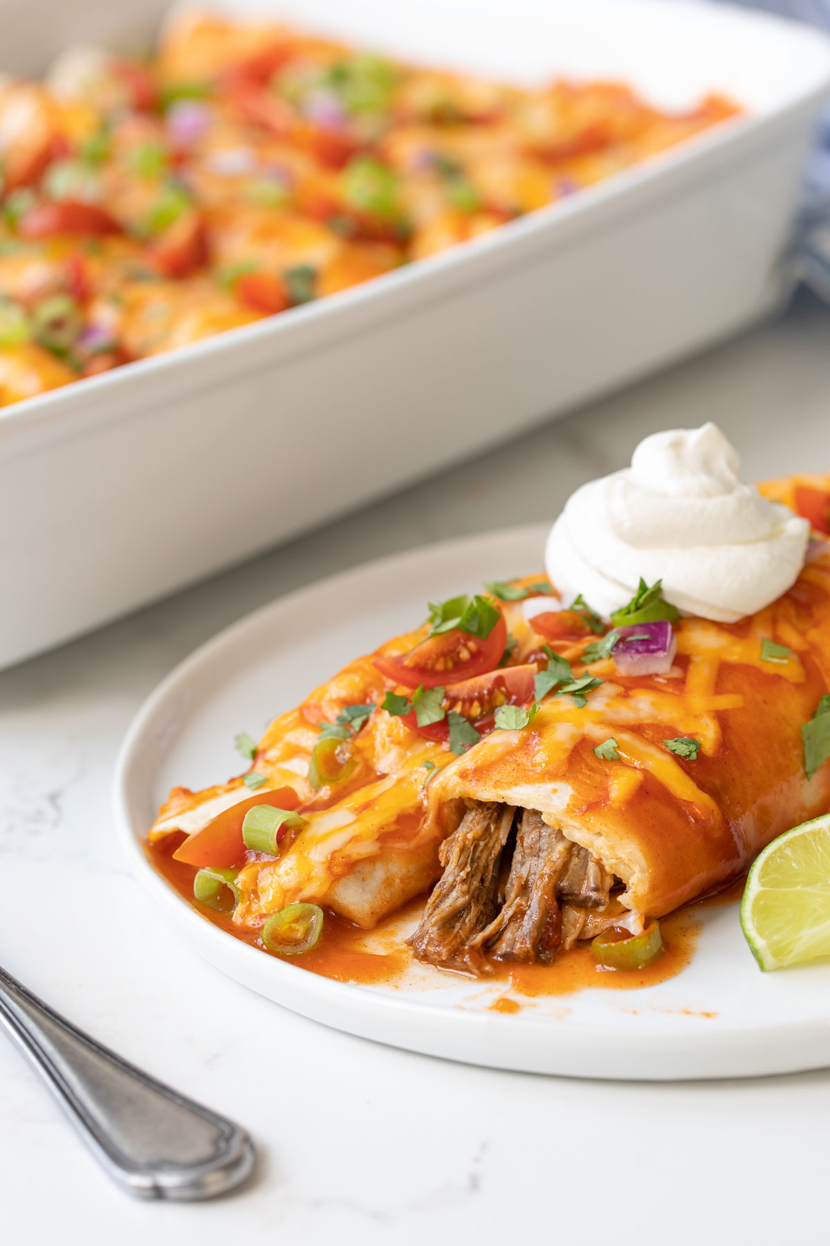 Two shredded beef enchiladas topped with sour cream on a white plate.