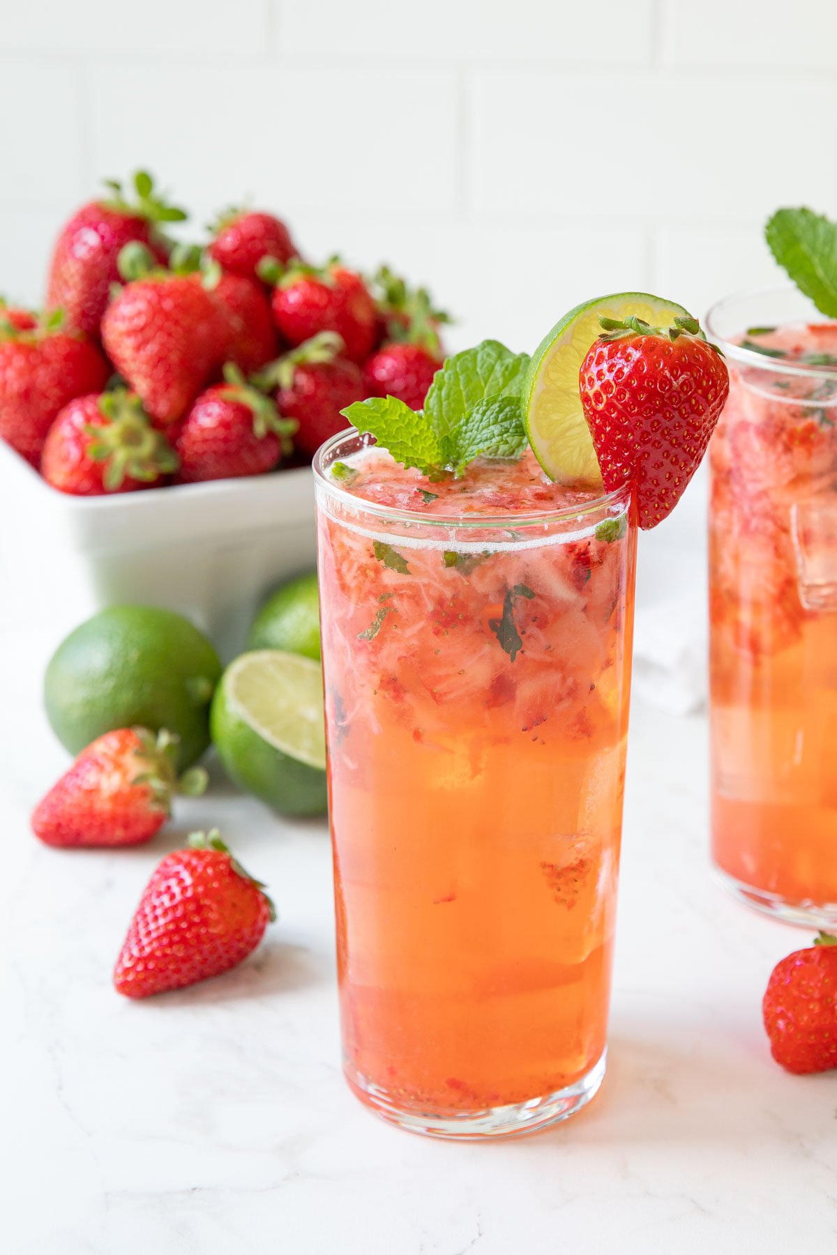 A strawberry mojito cocktail in a glass garnished with mint, a strawberry and lime wheel.