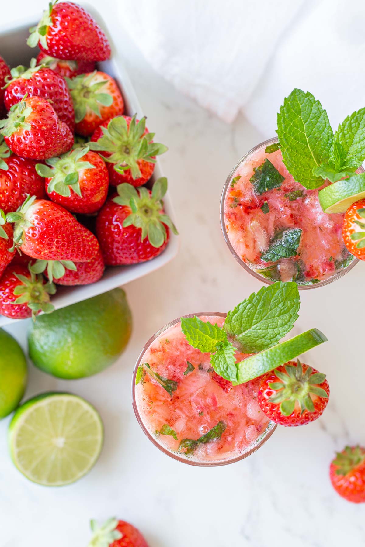 Overhead view of two strawberry mojitos by a container of fresh strawberries.