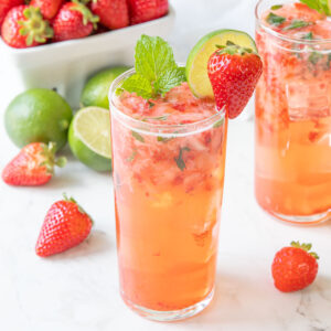 A strawberry mojito garnished with a fresh strawberry, lime wheel and fresh mint.