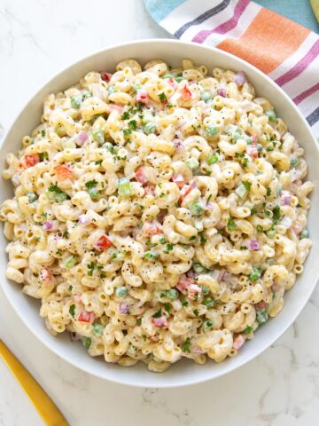 Classic macaroni salad in a white bowl by a striped dish towel.