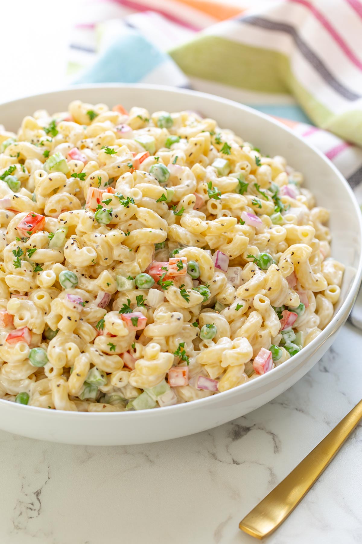 Front view of a bowl of macaroni salad by a gold serving spoon.