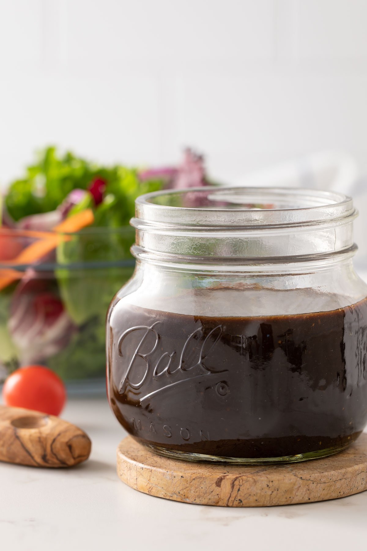 Front view of a jar of balsamic vinaigrette with a salad in the background.