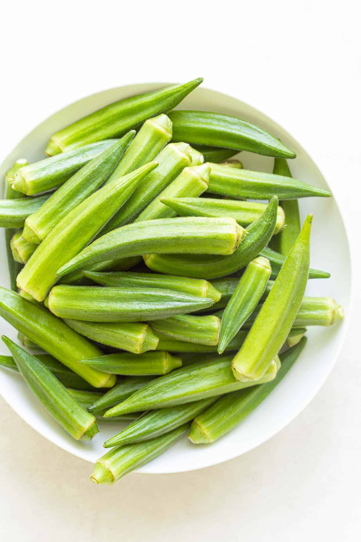 Overhead view of fresh okra pods in a white bowl.
