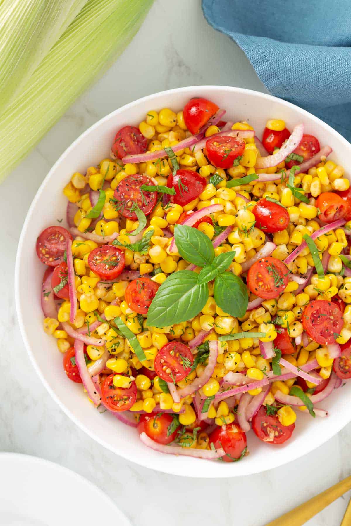 Corn Tomato salad garnished with fresh basil in a white bowl.