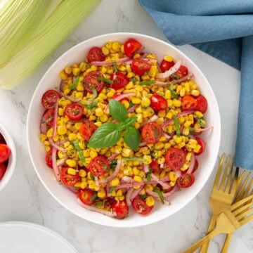 Corn and tomato salad in a white bowl beside three gold forks.