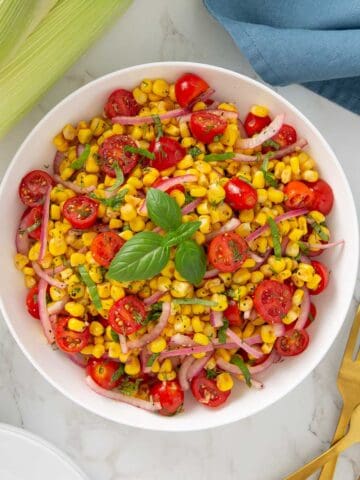 Corn and tomato salad in a white bowl beside three gold forks.