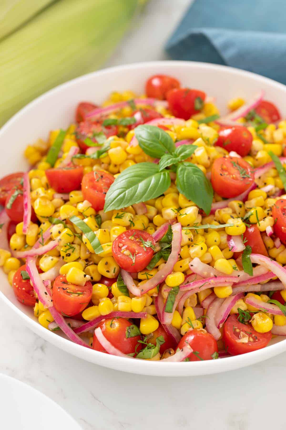 Closeup view of a bowl of corn and tomato salad with red onion and basil.