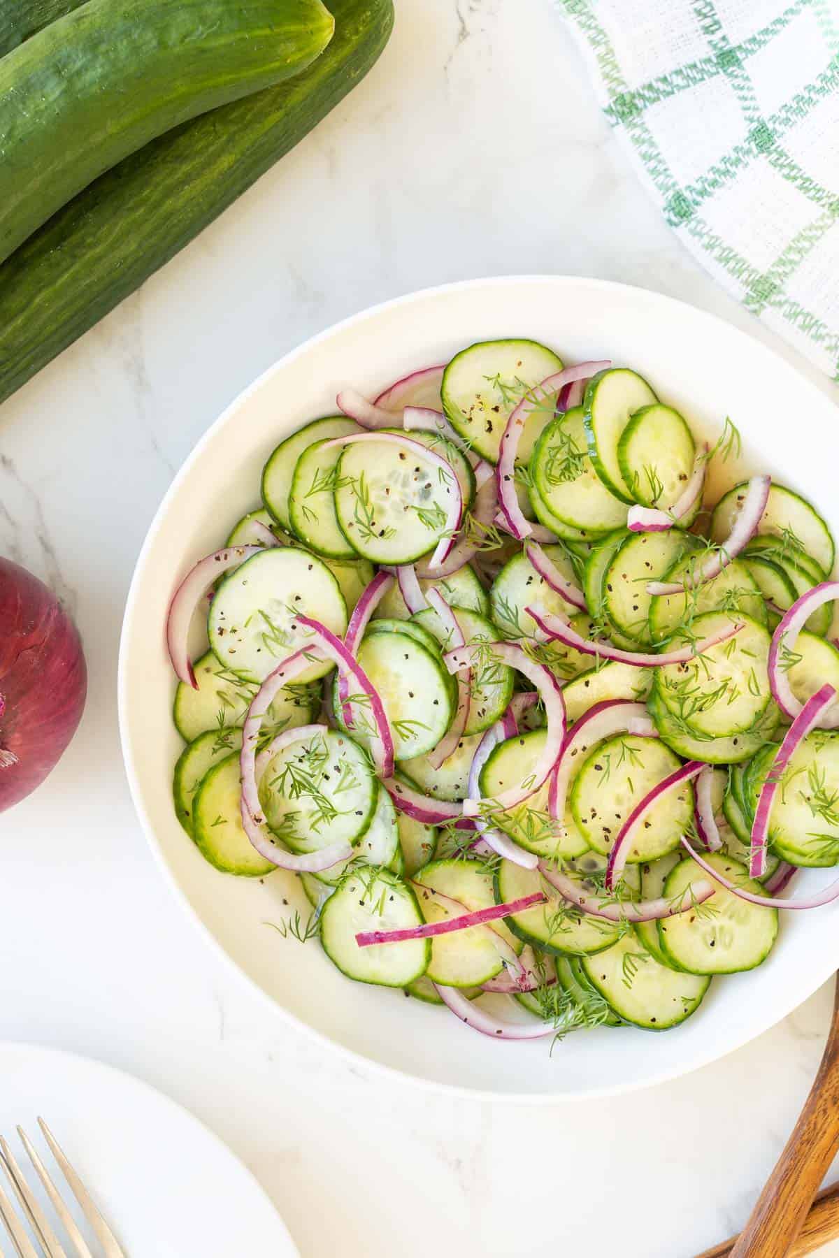 Cucumber onion salad in a white bowl beside a green and white dish towel.