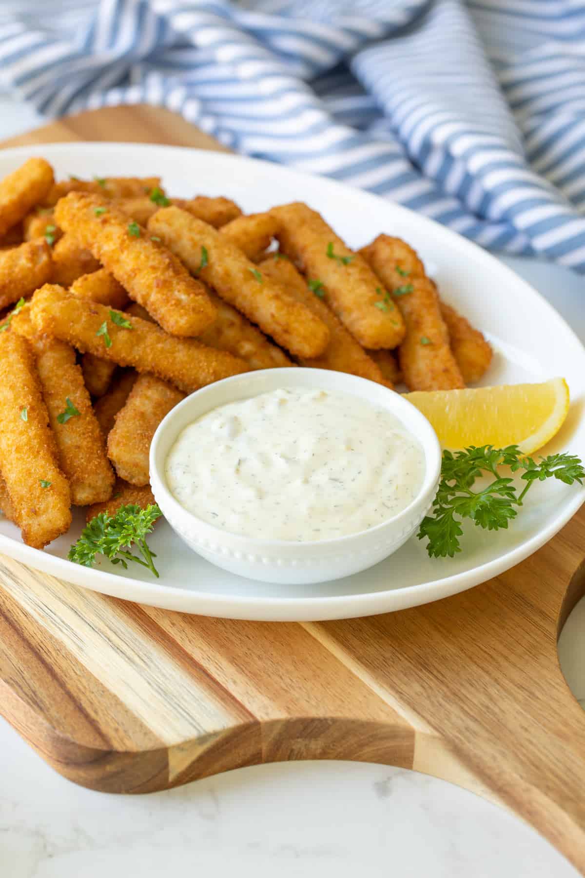 Front view of a bowl of homemade tartar sauce on a white platter with fish sticks.
