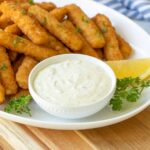 Closeup view of a white bowl of tartar sauce on a platter with fish sticks.