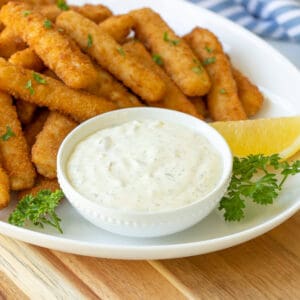 Closeup view of a white bowl of tartar sauce on a platter with fish sticks.