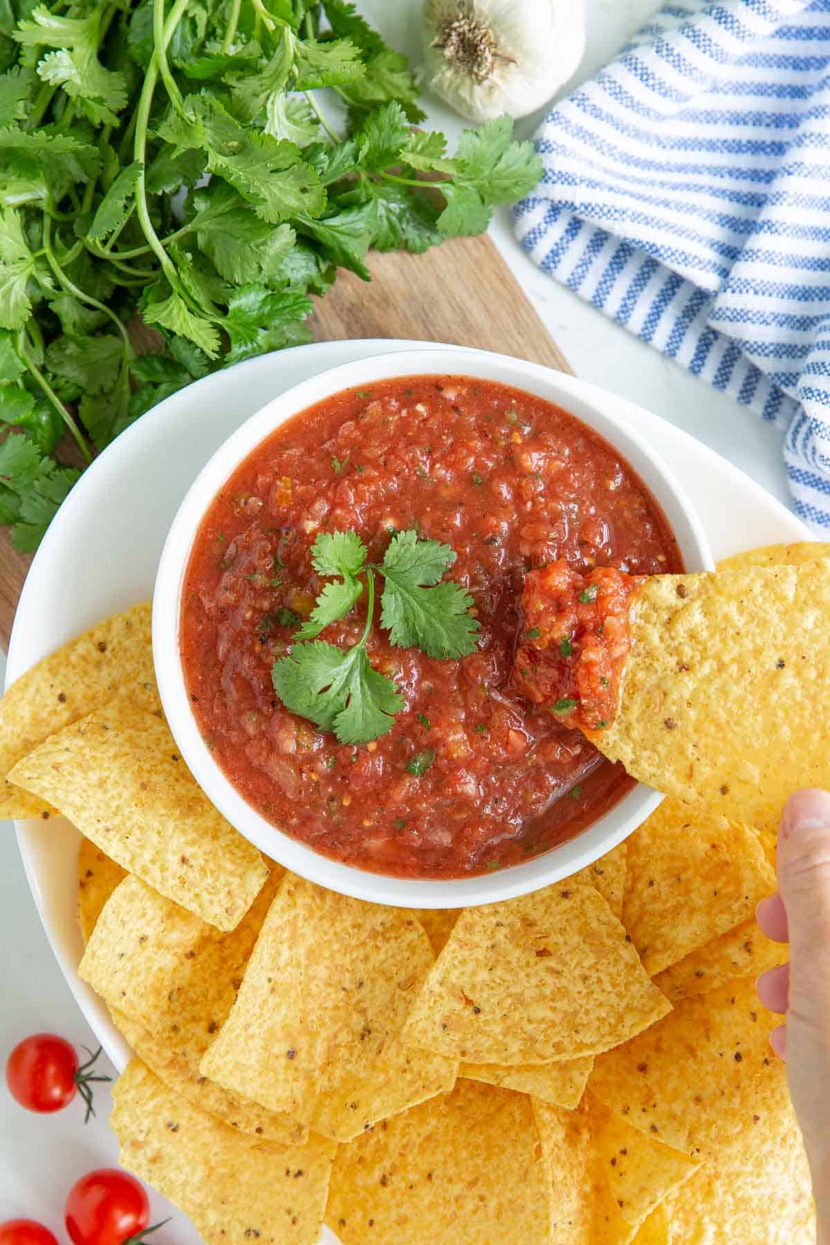 A tortilla chip being dipped into a bowl of blender salsa.