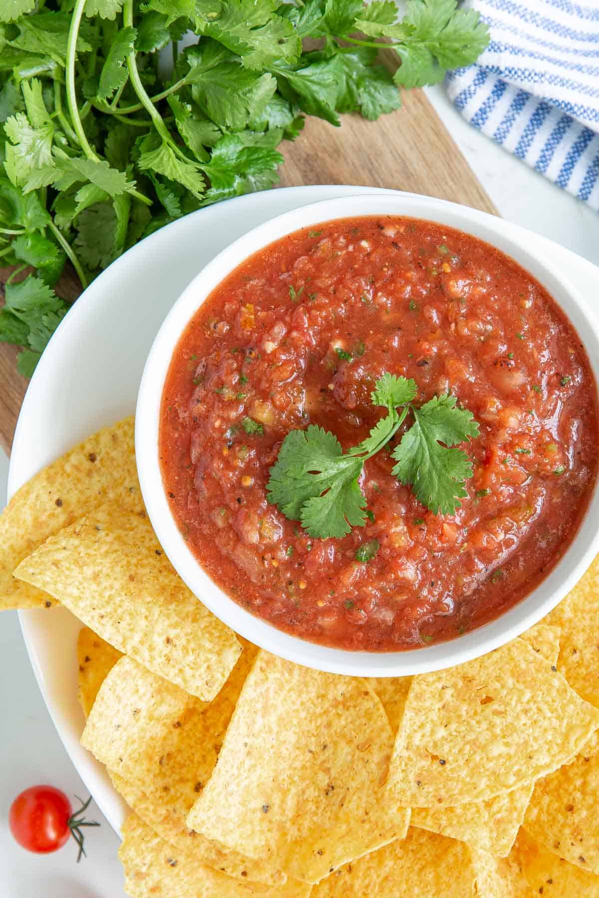 Overhead view of blender salsa in a white bowl surrounded by tortilla chips.