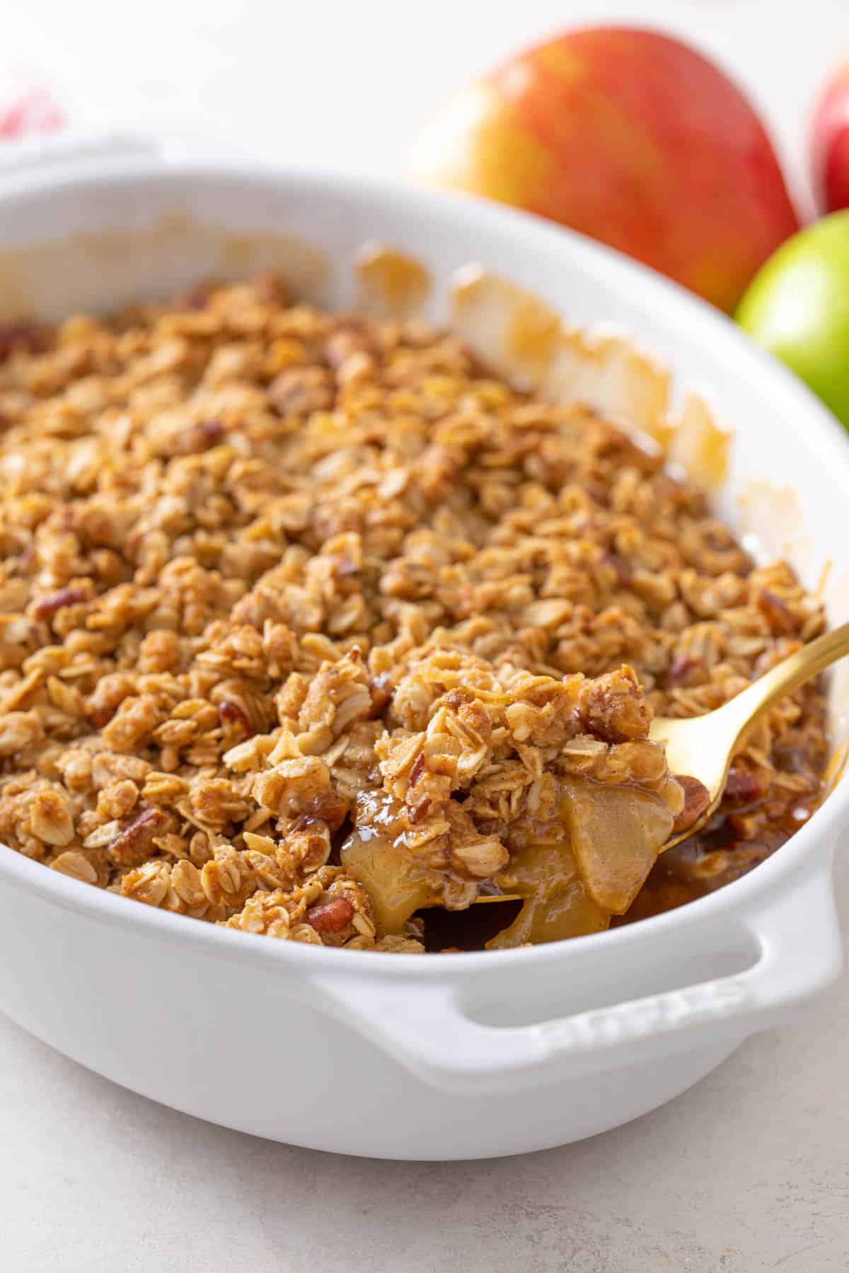 A spoon scooping apple crisp from a white baking dish.
