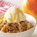 Front view of apple crisp in a bowl topped with ice cream. Overlay text at top of image.
