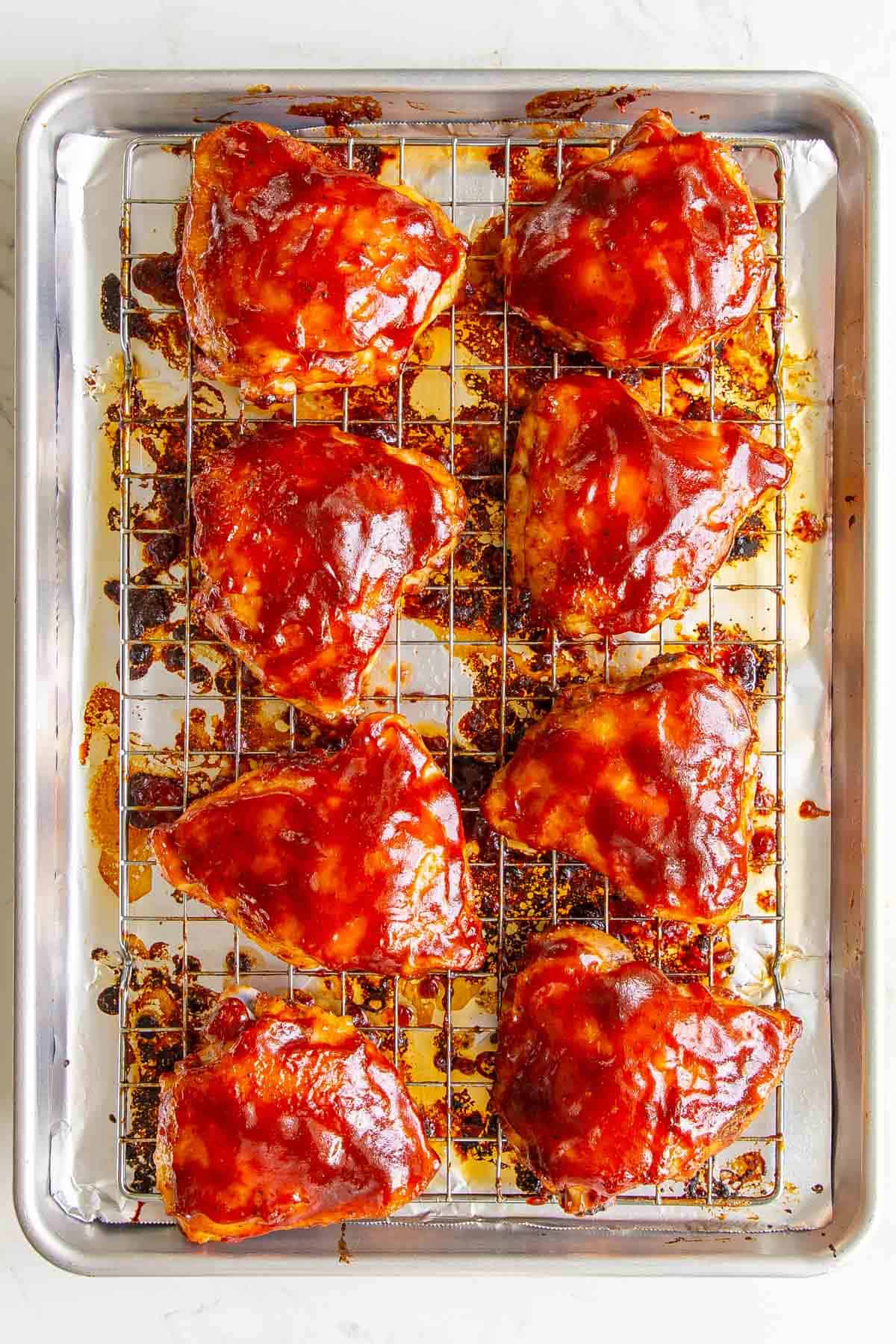 Overhead view of baked BBQ chicken thighs on a wire rack in a baking sheet.