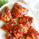 BBQ chicken thighs on a platter. Overlay text at top of image.