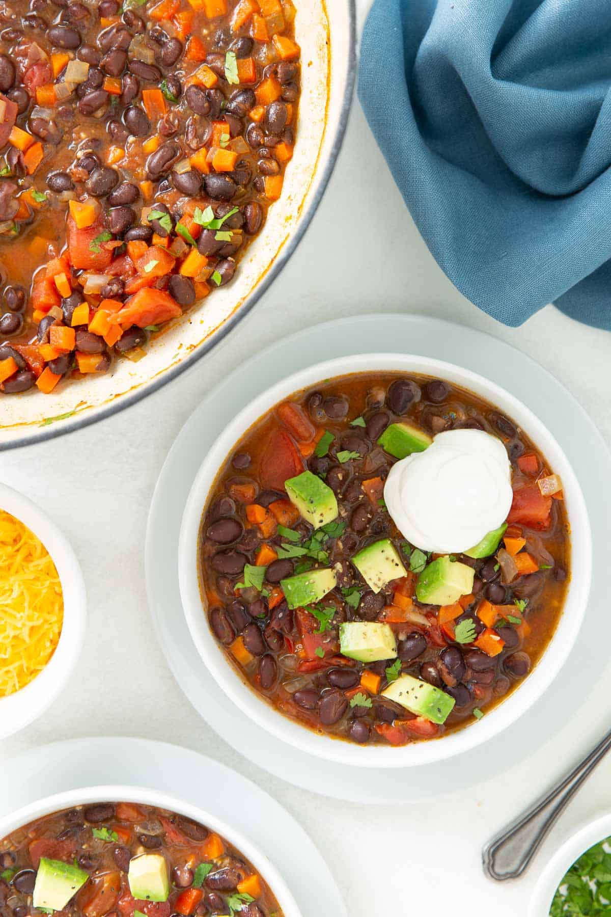 Black bean soup in a white bowl topped with avocado and sour cream.