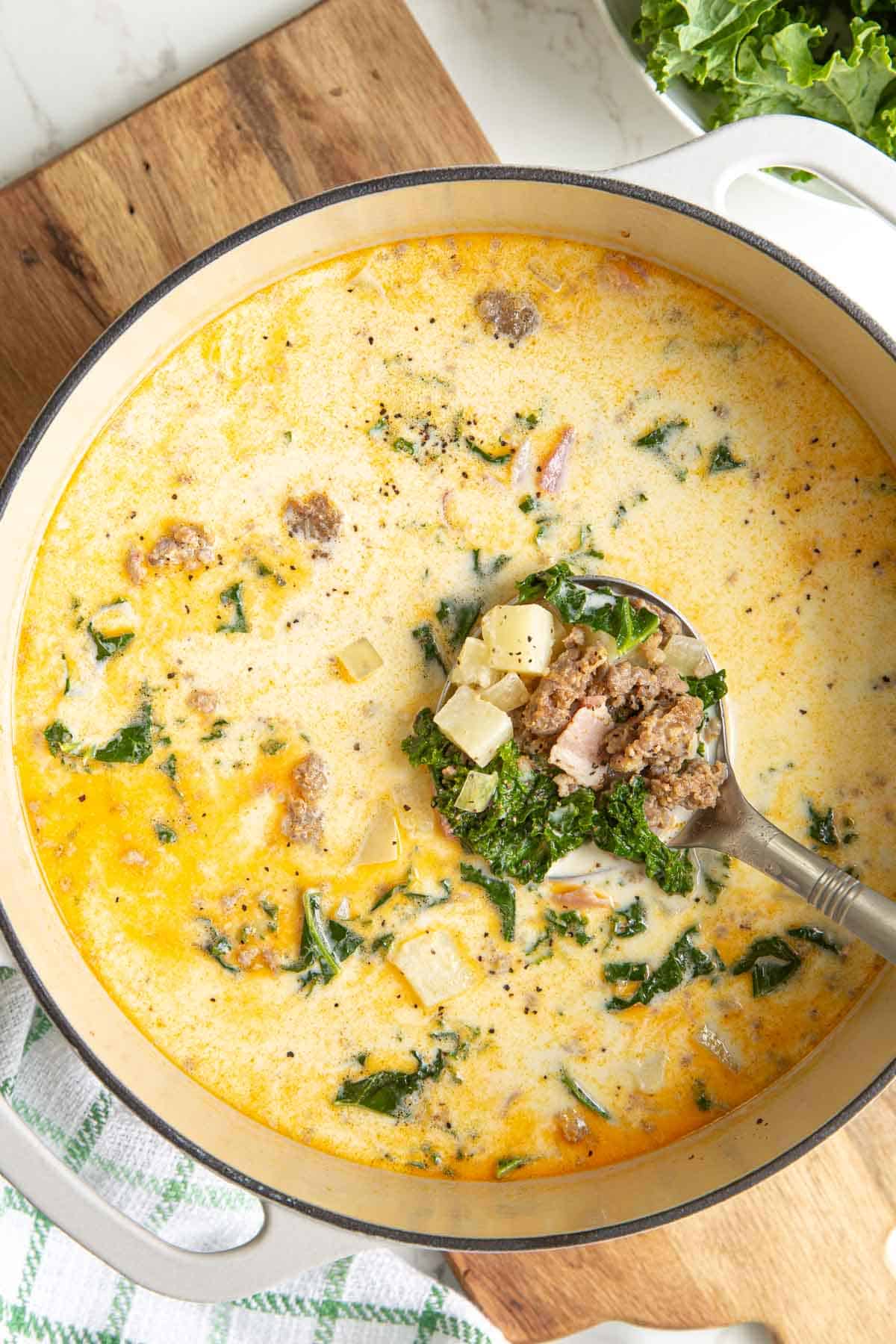 A stainless ladle ladling Zuppa Toscana soup from a white Dutch oven.