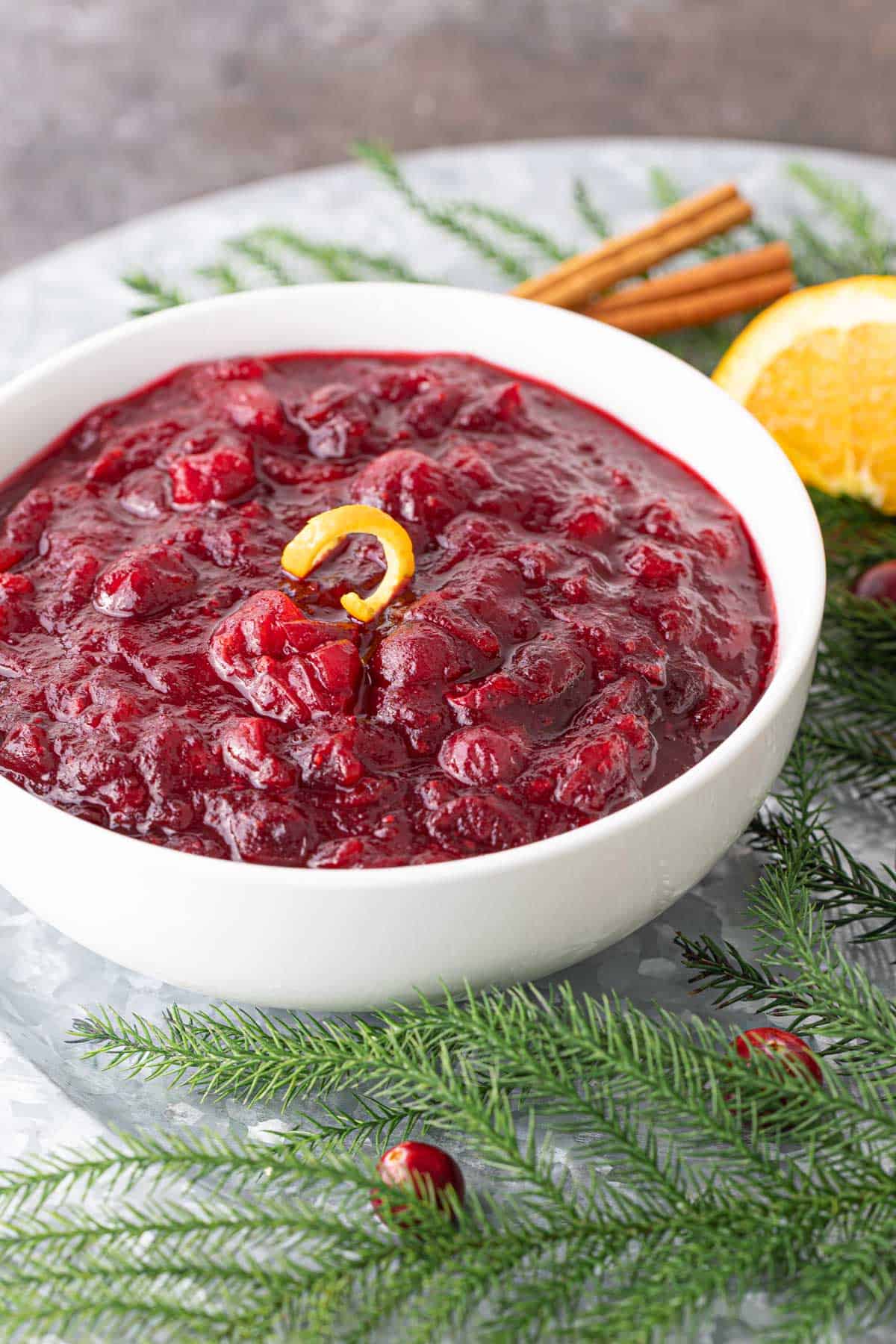 Front view of a bowl of cranberry sauce on a platter with greenery.