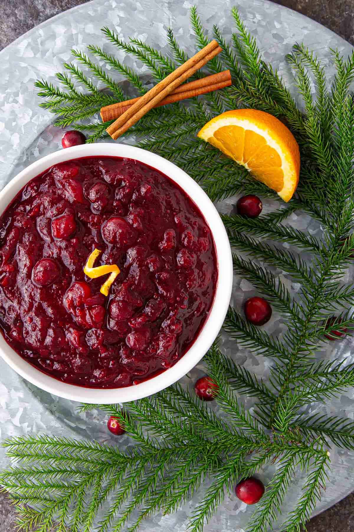 Overhead view of cranberry sauce on a platter with festive holiday greenery and fresh cranberries.