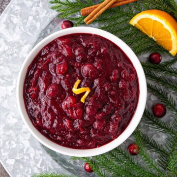 A white bowl of cranberry sauce garnished with orange peel.