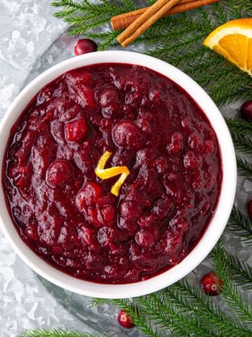 A white bowl of cranberry sauce garnished with orange peel.