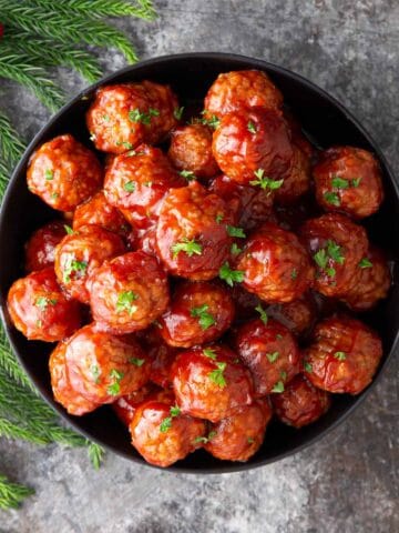 Crock pot cranberry meatballs in a black bowl garnished with parsley.