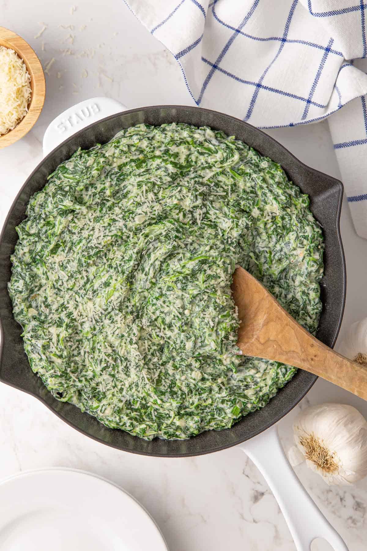 Creamed spinach sprinkled with grated Parmesan in a skillet.
