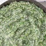 Overhead closeup view of creamed spinach in a white skillet. Overlay text at top of image.
