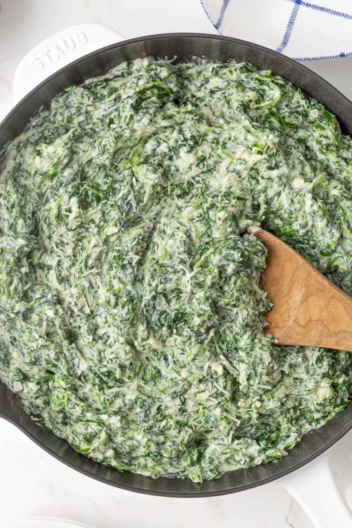 A wooden serving spoon in a skillet of creamed spinach.