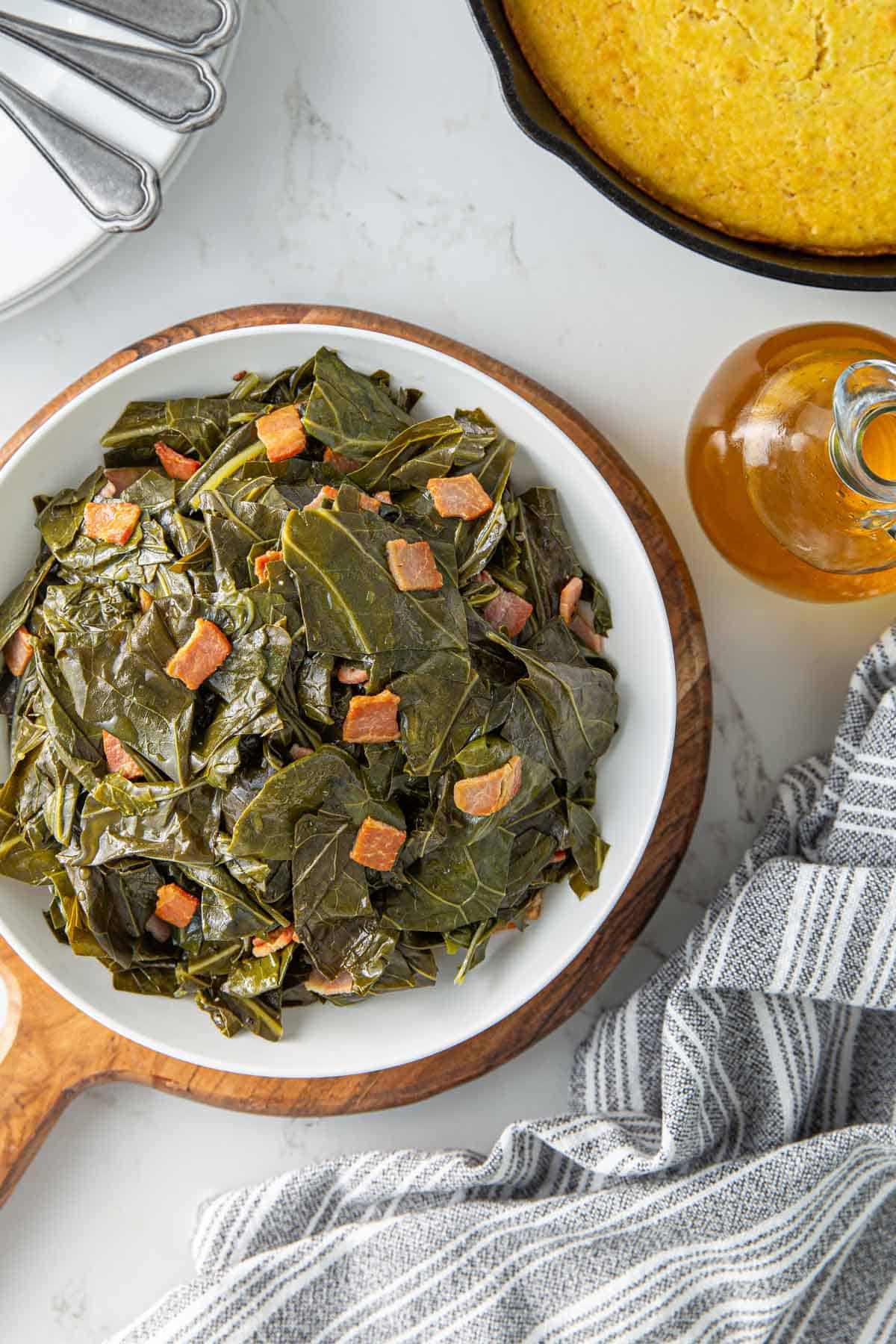 Overhead view of a bowl of collards by a skillet of cornbread and a bottle of vinegar.