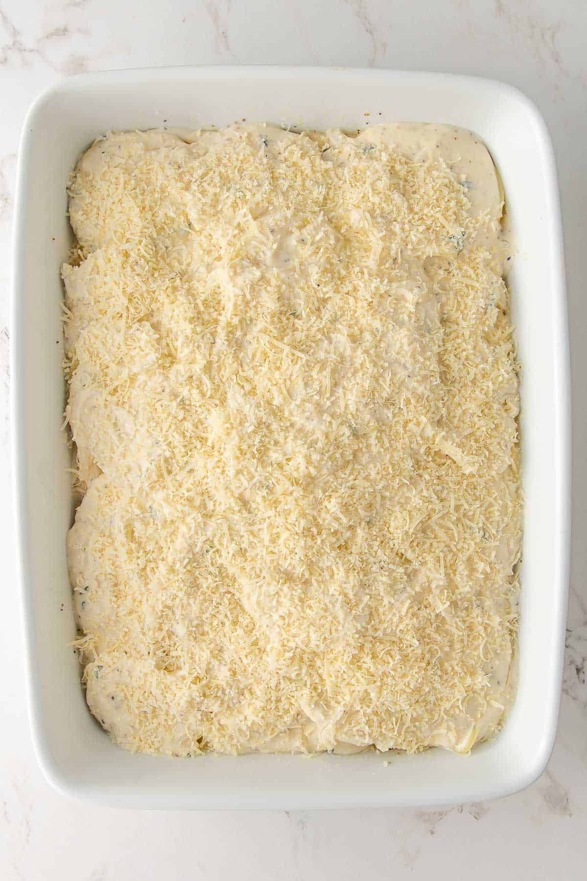 Overhead view of a dish of unbaked scalloped potatoes sprinkled with Parmesan.