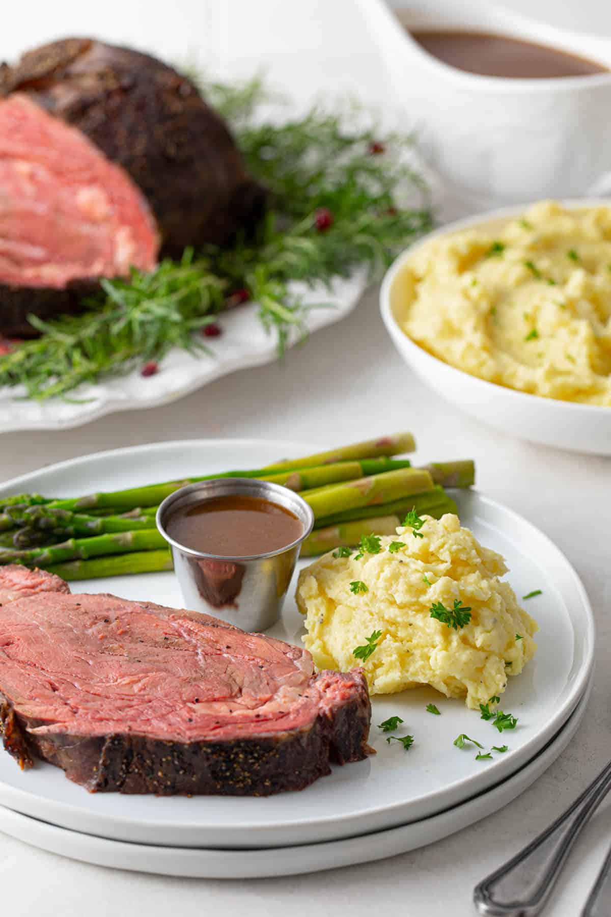 A plate with a slice of boneless prime rib with au jus, mashed potatoes and asparagus.