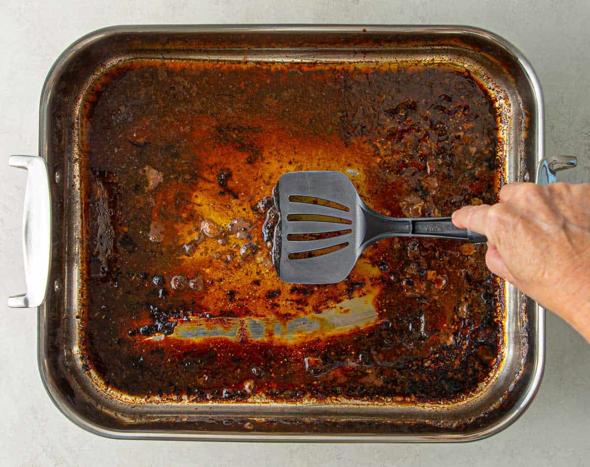 A spatula scraping pan drippings with beef broth in a roasting pan.