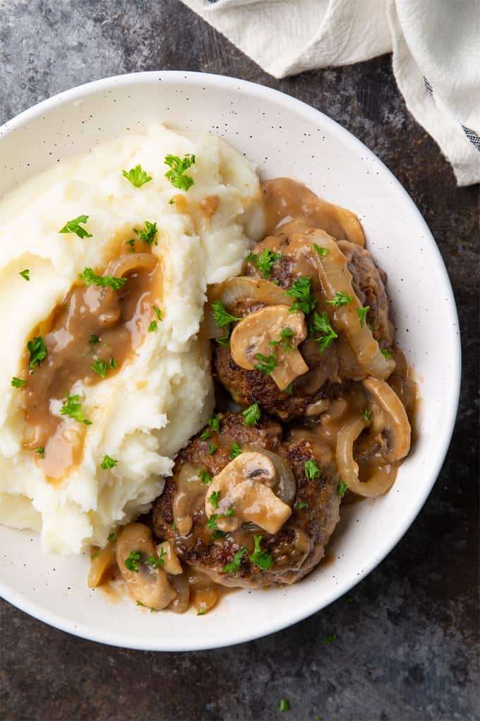 Overhead view of hamburger steak and gravy with mashed potatoes in a white bowl.