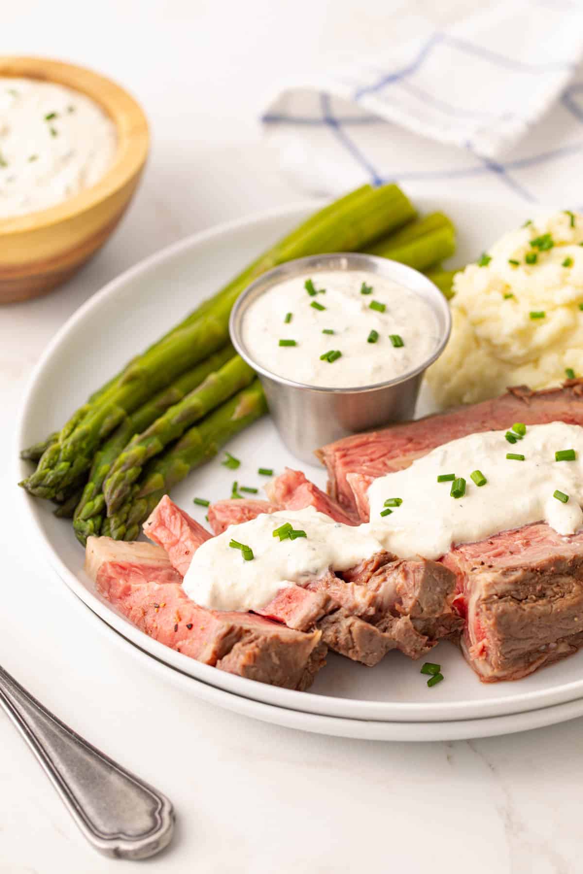 Prime rib on a white plate topped with homemade horseradish sauce.