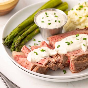 Prime rib on a white plate topped with horseradish sauce.